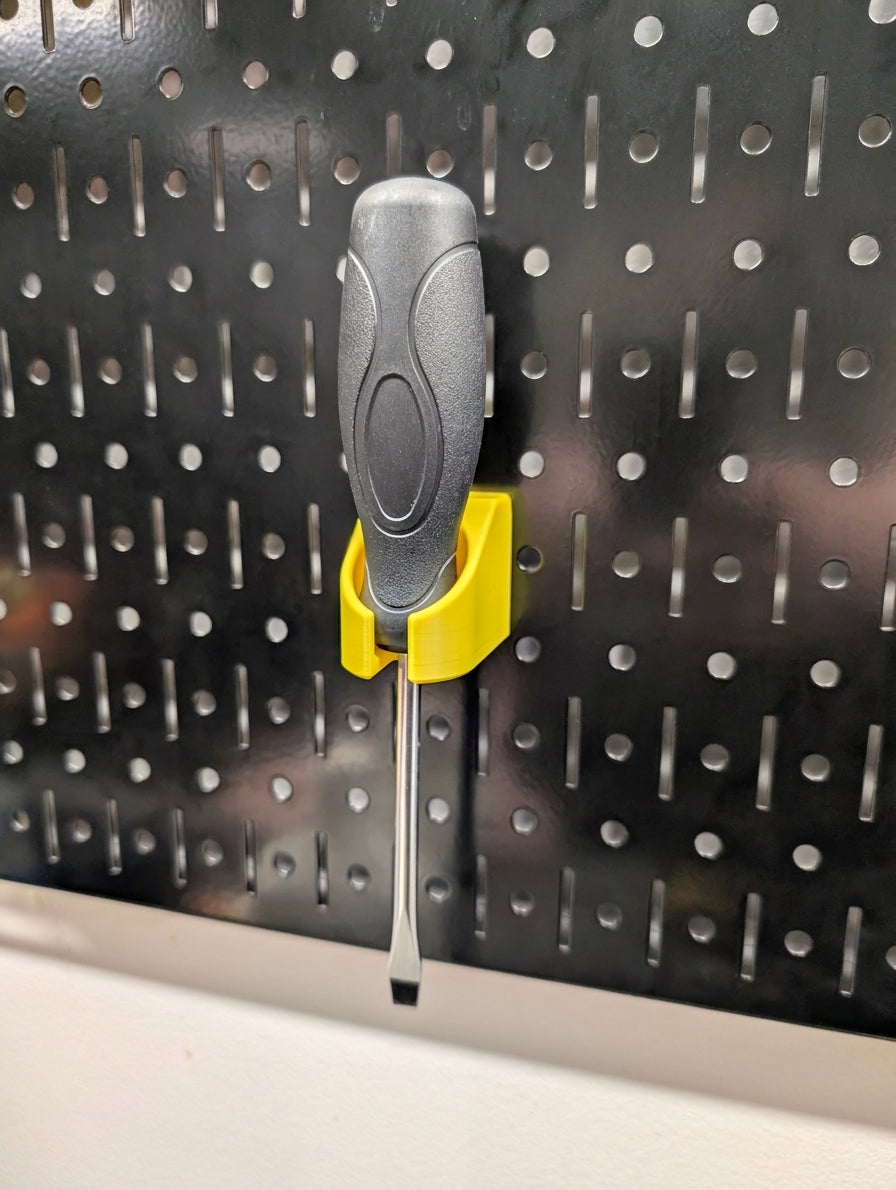 A gray and black screwdriver with a yellow plastic holder on a black Wall Control pegboard panel.