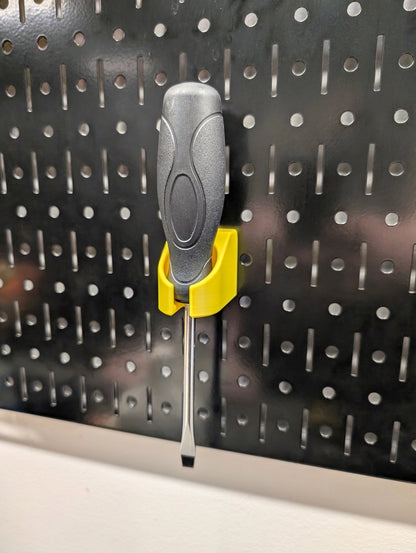 A gray and black screwdriver with a yellow plastic holder on a black Wall Control pegboard panel.