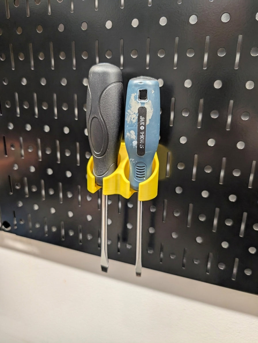 Two screwdrivers with black and blue handles are stored in a yellow plastic pegboard holder mounted on a black metal Wall Control pegboard.