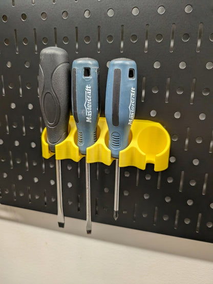 A yellow plastic screwdriver rack mounted on a black Wall Control pegboard, holding three screwdrivers with gray and blue handles.